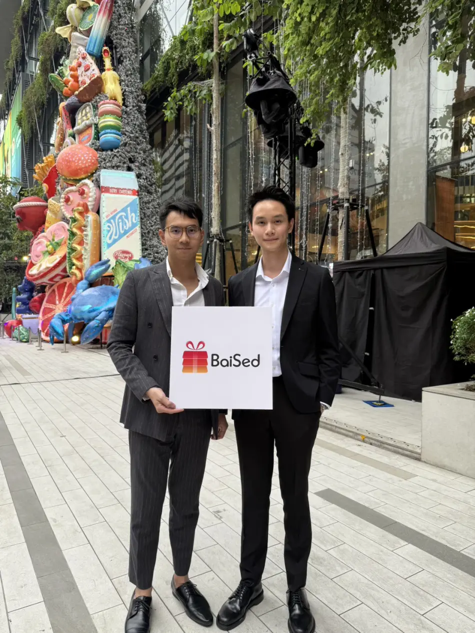 Two of the BaiSed team outside a Bangkok mall holding a BaiSed logo board